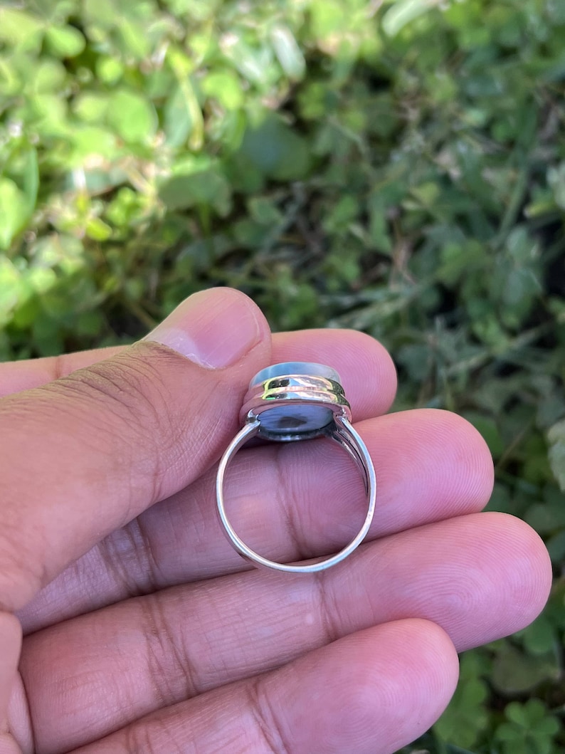 Op de afbeelding: Een zilveren ring met een lichtblauwe ovale edelsteen in een bezel-setting.