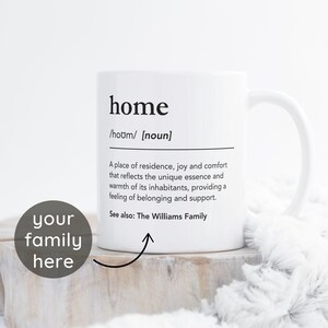 Può includere: Una tazza in ceramica bianca con una definizione in nero della parola "home" stampata su di essa. La definizione recita: "Un luogo di residenza, gioia e conforto che riflette l'essenza unica e il calore dei suoi abitanti, fornendo un senso di appartenenza e supporto. Vedi anche: La famiglia Williams."