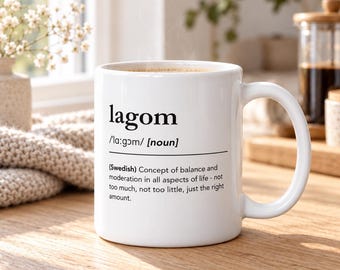 Könnte beinhalten: Ein weißer Keramikbecher mit dem schwarz aufgedruckten Text lagom, der phonetischen Aussprache, der Klassifizierung als Substantiv und der Definition: Schwedisches Konzept von Ausgewogenheit und Mäßigung in allen Lebensbereichen.