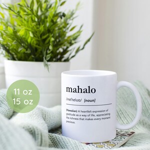 Puede incluir: Taza de cerámica blanca con un diseño negro que dice "mahalo" y su definición. La taza es de 11 oz o 15 oz.