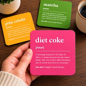 Puede incluir: Tres posavasos cuadrados con esquinas redondeadas que presentan definiciones al estilo de un diccionario. Uno es rosa brillante etiquetado diet coke, uno amarillo etiquetado piña colada y uno verde etiquetado matcha. Cada uno incluye la etiqueta sustantivo y una definición.