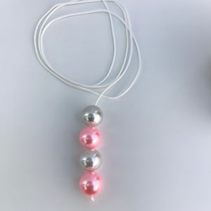 May include: A necklace with a white cord and four beads. The beads alternate silver and pink.