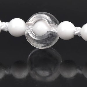 May include: A close-up of a white plastic beaded chain with a clear plastic connector. The beads are round and smooth.