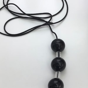 May include: A black beaded necklace featuring three large, glossy, spherical beads. The beads are separated by silver-coloured metal tubes and strung on a black cord. The necklace is shown against a white background.