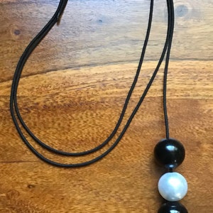 May include: A black cord necklace with three beads. The beads are black, white, and black.