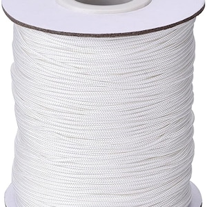 Puede incluir: Una bobina de cordón blanco, enrollada firmemente en un tubo de cartón. El cordón es liso y parece estar hecho de nylon.
