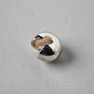 Pode incluir: Uma conta de metal prateada com uma abertura de anel partido. A conta é projetada para ser usada como fecho ou conector para a fabricação de joias.