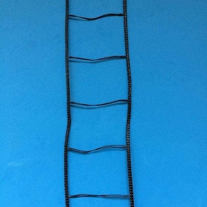 Może przedstawiać: Czarny sznurek w kształcie drabiny z sześcioma szczeblami na niebieskim tle.