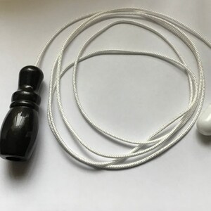 May include: A black wooden pull with a white cord and a white plastic end. The cord is coiled up on a white surface.