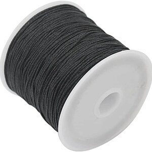 Pode incluir: Uma bobina de cordão encerado preto, enrolada em torno de uma bobina de plástico branco.