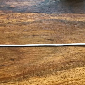 Può includere: Catenella di trazione per ventilatore a soffitto bianca con pomo in legno. La catena è collegata a una presa per catenella di trazione per ventilatore a soffitto in plastica bianca.