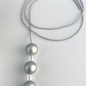 May include: A silver cord with three silver beads attached. The cord is looped and the beads are hanging down.