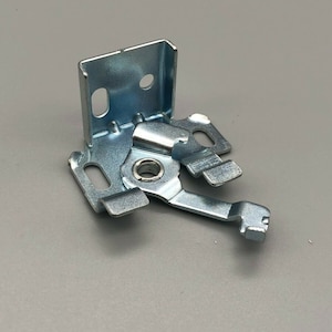 Puede incluir: Un soporte de metal plateado con una pequeña palanca de metal. El soporte tiene dos agujeros y la palanca tiene un pequeño pasador de metal.