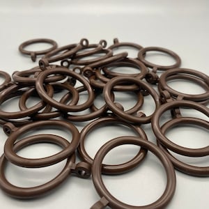 May include: A pile of brown plastic curtain rings. The rings are about 1 inch in diameter and have a small hook on one side.