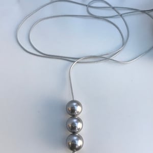 Puede incluir: Un collar plateado con tres cuentas grandes, redondas y plateadas.