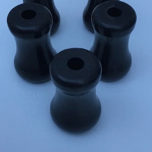 Puede incluir: Cinco pomos de plástico negro con parte superior redonda y base cilíndrica.