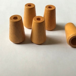 May include: Five wooden lamp finials in a light brown color. The finials are cone-shaped with a hole in the top.