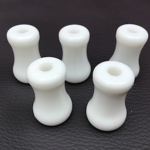 Puede incluir: Cinco tiradores de plástico blanco con un agujero redondo en el centro. Los tiradores son lisos y tienen una forma ligeramente redondeada.