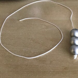 May include: A white string with three silver beads attached to the end.