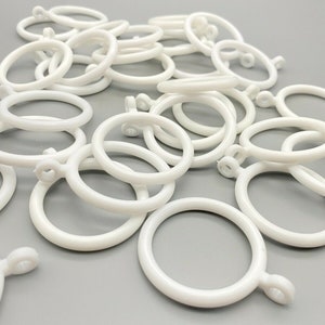 May include: A pile of white plastic curtain rings. The rings are about 1 inch in diameter and have a small hook on one side.