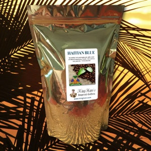 May include: A shiny, metallic bag of Haitian Blue coffee. The label features the text "HAITIAN BLUE" and a description of the coffee's qualities. The label also includes an image of coffee beans and leaves, and the brand name "King Hari's Imperial Coffees".