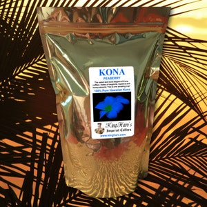 May include: A metallic silver bag of Kona Peaberry coffee. The label reads "Kona Peaberry" and describes the coffee's notes of magnolia, hazelnut, and honey. The label also features a blue flower and the text "100% Pure Hawaiian Kona."