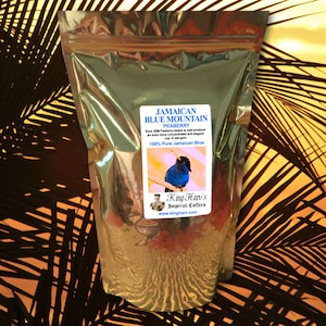 May include: A shiny, metallic bag of Jamaican Blue Mountain Peaberry coffee. The bag has a label with text and an image of a blue bird. The text reads "100% Pure Jamaican Blue". The background has a tropical theme.