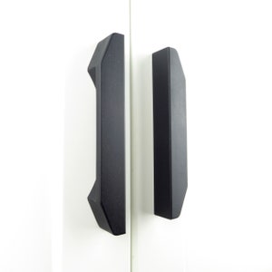 May include: Two black cabinet door pulls with a geometric design. The pulls are made of metal and have a matte finish.