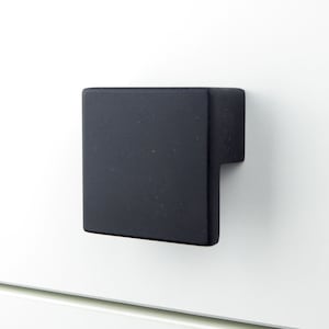 May include: Black square cabinet pull with a rectangular cutout. The pull is made of metal and has a matte finish.