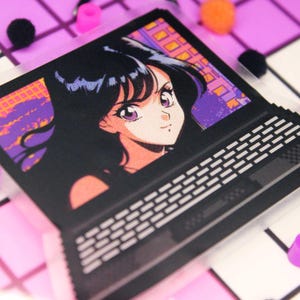 Pixel art retro anime girl sticker on a laptop with a clear backing.