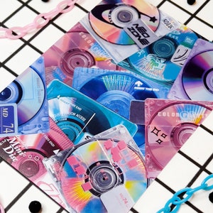 May include: A collection of colorful mini-discs and CDs with text like "MD 74" and "Neo Zone". The discs are in shades of pink, blue, and purple, with a grid background and pink and blue chain accents.