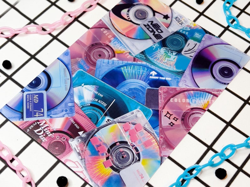 May include: A collection of colorful mini-discs and CDs with text like "MD 74" and "Neo Zone". The discs are in shades of pink, blue, and purple, with a grid background and pink and blue chain accents.
