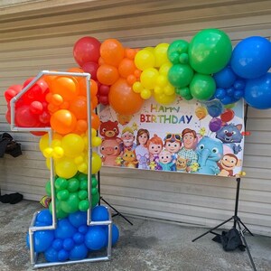 Puede incluir: Un arco de globos arco&iacute;ris con una pancarta que dice "Feliz cumplea&ntilde;os" y una gran escultura de globos n&uacute;mero uno hecha de globos en un patr&oacute;n arco&iacute;ris.