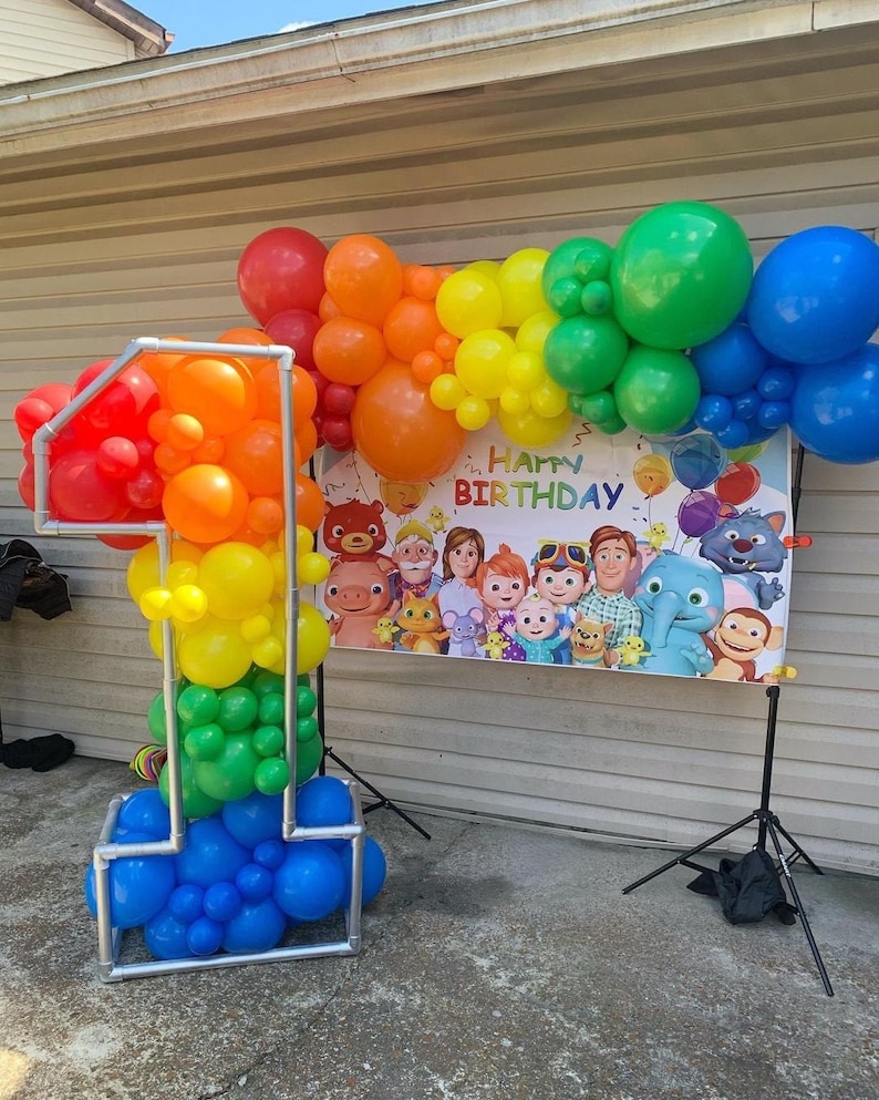 Puede incluir: Un arco de globos arco&iacute;ris con una pancarta que dice "Feliz cumplea&ntilde;os" y una gran escultura de globos n&uacute;mero uno hecha de globos en un patr&oacute;n arco&iacute;ris.