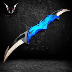 Puede incluir: Un cuchillo plegable azul y negro con un mango en forma de murci&eacute;lago. La hoja est&aacute; parcialmente abierta y tiene un borde dentado.