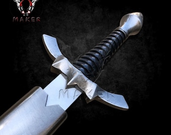 May include: A silver and black dagger with a pointed blade and a textured black handle. The hilt has a crossguard with decorative points. The word "MAKER" is etched on the blade. The dagger is set against a dark background.