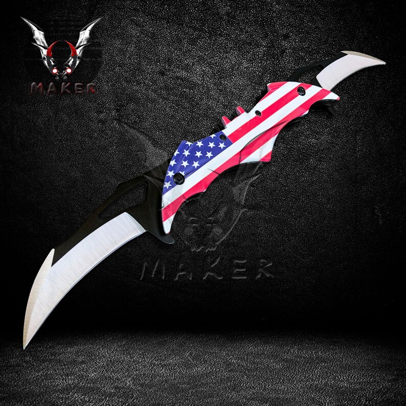 Puede incluir: Un cuchillo plegable negro y plateado con un mango en forma de murci&eacute;lago. La hoja est&aacute; decorada con la bandera estadounidense.