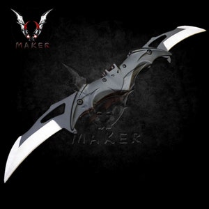 Puede incluir: Un cuchillo plegable negro y plateado con un dise&ntilde;o en forma de murci&eacute;lago. El cuchillo tiene dos hojas y un mango negro.