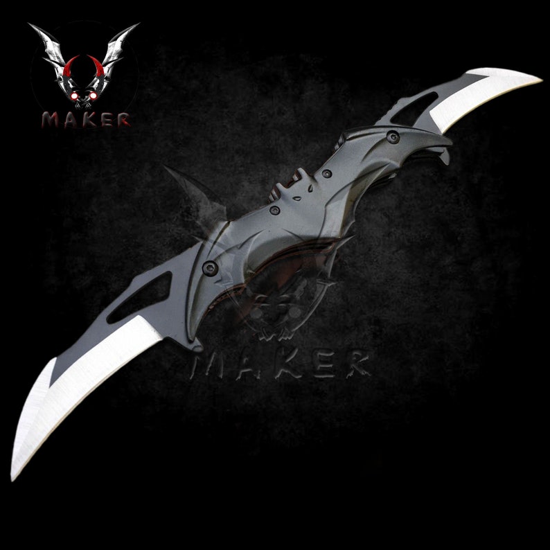 Puede incluir: Un cuchillo plegable negro y plateado con un dise&ntilde;o en forma de murci&eacute;lago. El cuchillo tiene dos hojas y un mango negro.