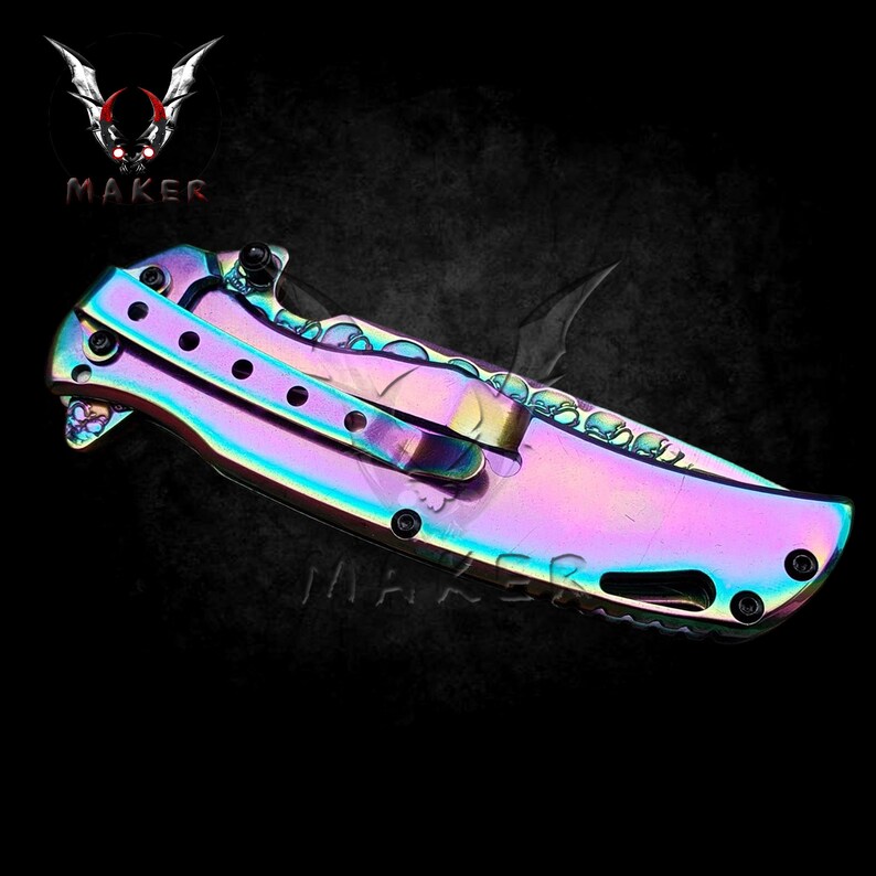 May include: A rainbow-coloured folding knife with a skull pattern on the handle. The blade is partially open and has a black handle.