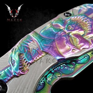 May include: A rainbow iridescent pocket knife with a skull design. The knife has a detailed skull design on the handle and blade.