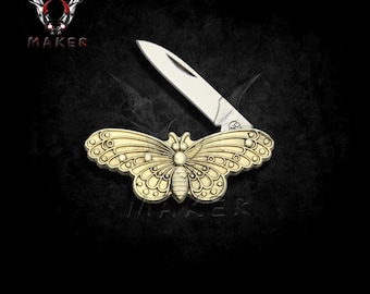 Puede incluir: Una navaja de bolsillo dorada con un diseño de mariposa en el mango. La hoja plateada está abierta. La palabra "MAKER" está impresa en rojo en la esquina superior izquierda de la imagen.