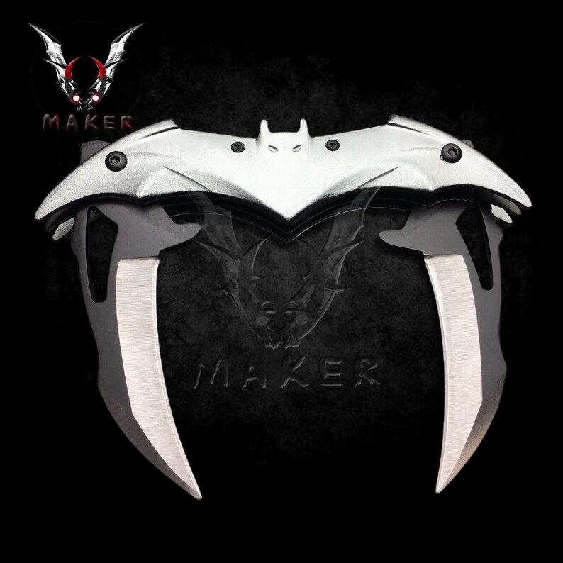 Puede incluir: Un cuchillo plegable plateado y negro con un mango en forma de murci&eacute;lago. El cuchillo tiene dos hojas que son curvas y puntiagudas.