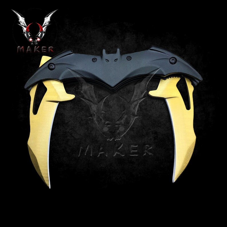 Puede incluir: Un cuchillo plegable negro y dorado con un mango en forma de murci&eacute;lago. El cuchillo tiene dos hojas que son curvas y puntiagudas.