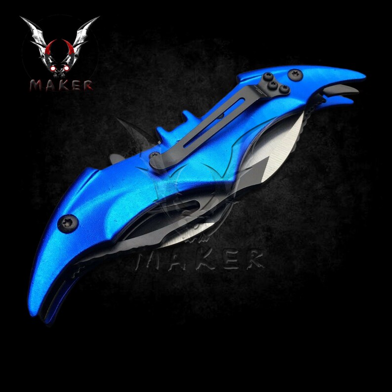 Puede incluir: Un cuchillo plegable azul y negro con forma de murci&eacute;lago. El cuchillo tiene un mango negro y una hoja azul. La hoja est&aacute; parcialmente abierta y el mango tiene un clip negro.