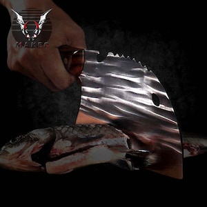 May include: A large, textured metal cleaver with a wooden handle is held over a fish. The cleaver has a unique, curved blade with a serrated edge and a hole near the top. The word "MAKER" is in the upper left corner.