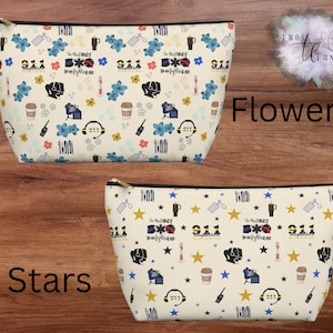 May include: Two cream-coloured zippered cosmetic bags with black trim. One bag features a floral pattern with blue flowers and the text "In the Family 911 Firefighter". The other bag has a star pattern.