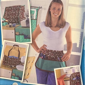 May include: Simplicity sewing pattern 2679, featuring a woman wearing an apron with a brown and white safety pin pattern. The pattern includes images of sewing projects and the text "ONE SIZE".