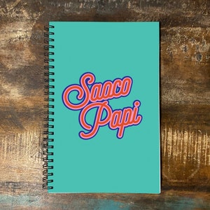 Könnte beinhalten: Ein türkisblaues Spiralnotizbuch mit den Worten "Saco Papi" in rot und blau.