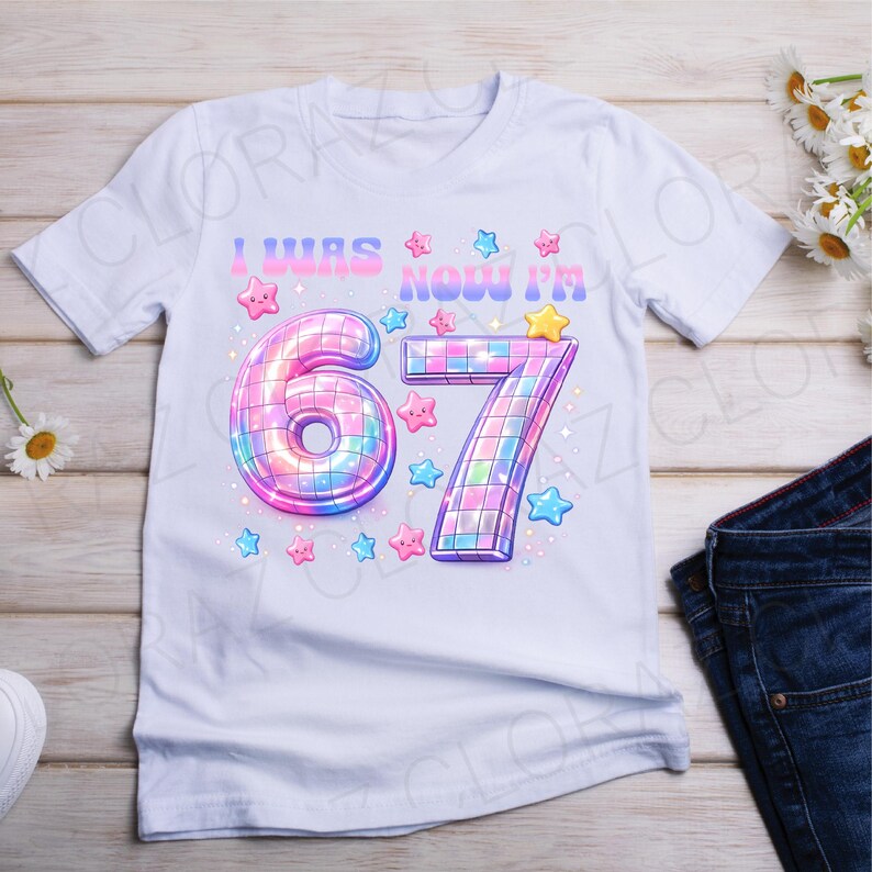 Pu&ograve; includere: T-shirt bianca con la scritta "I WAS NOW I'M" sopra i numeri "67". I numeri sono disegnati con un effetto palla da discoteca, circondati da stelle rosa, blu e gialle. Una divertente maglietta di compleanno.